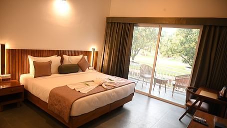 A double bed alongside a sliding window with an outside view at the Deluxe Cottage at Mango Leaf Lake Resort, Pune