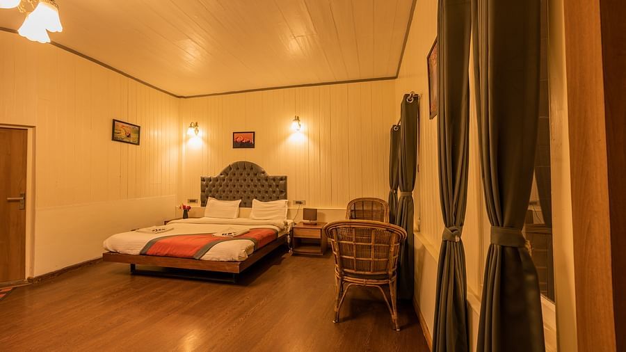 A eye bird view of a warmly lit spacious hotel room with a comfortable bed, a wall painting, and a cosy seating area, offering a homey atmosphere for guests- Arcadia Heritage Resort, Darjeeling