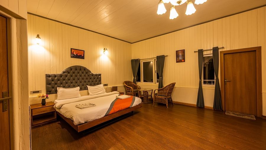  A warmly lit spacious hotel room with a comfortable bed, a wall painting  and a cosy seating area, offering a homey atmosphere for guests- Arcadia Heritage Resort, Darjeeling
