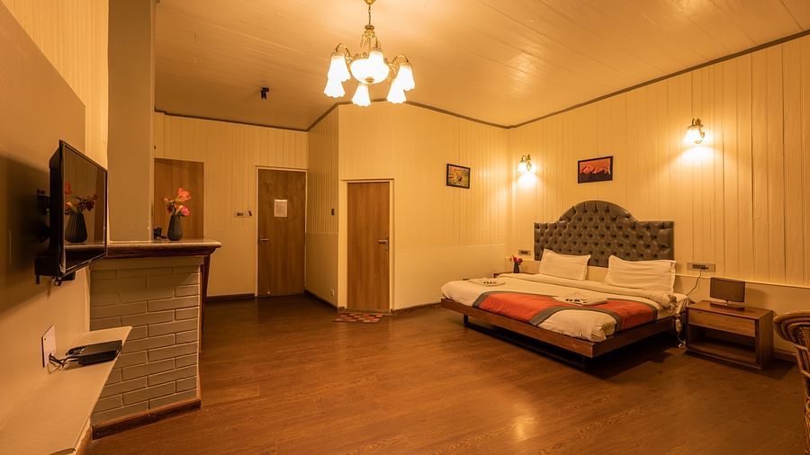  A side angle view of a warmly lit spacious hotel room with a comfortable bed, a flat-screen TV, and a cosy seating area, offering a homey atmosphere for guests- Arcadia Heritage Resort, Darjeeling