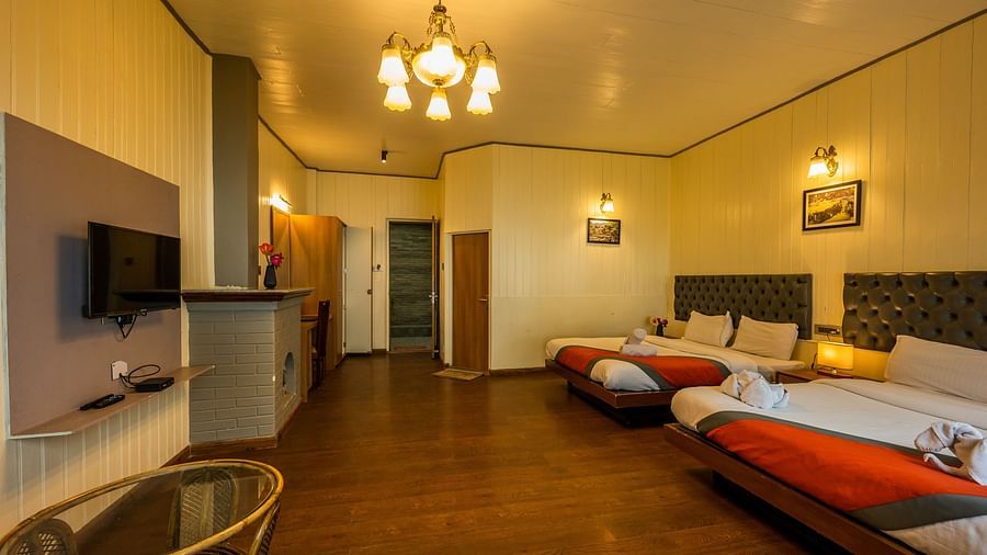 A side corner view of  spacious family room with 2 comfy beds, table, chimney at Arcadia Heritage Resort, Darjeeling