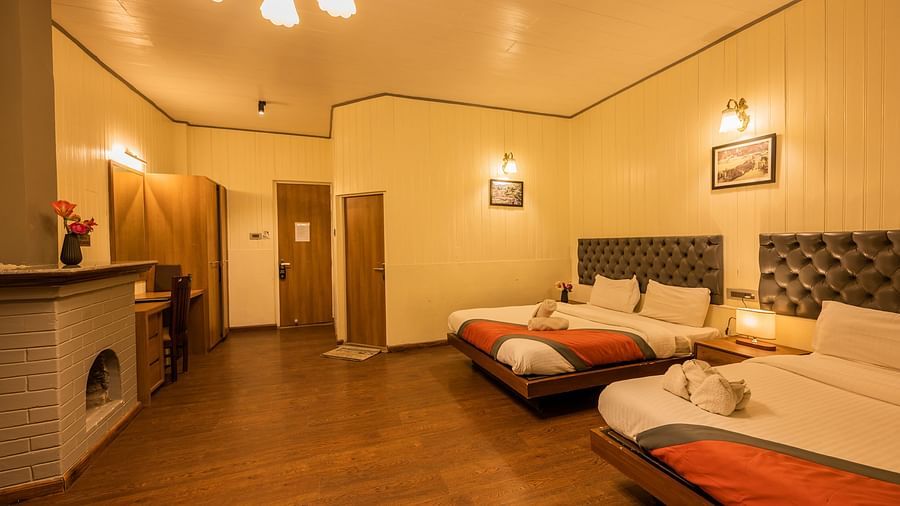 A side corner view of  spacious family room with 2 comfy beds, table, chimney at Arcadia Heritage Resort, Darjeeling