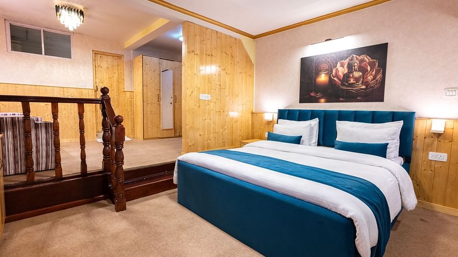 Image of suite featuring plush bed with duvet, pillows and cushions under mood lighting and a wall art of Buddha hanging over the headboard