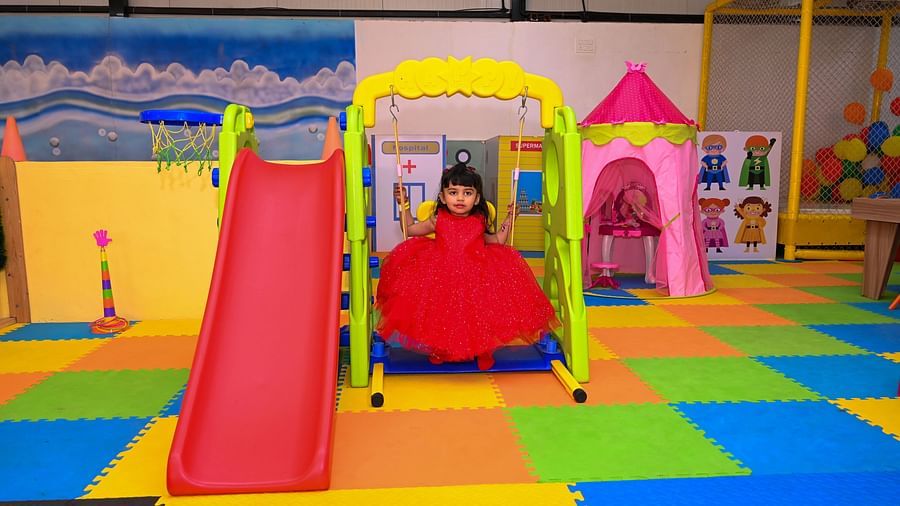 Young child in a red dress playing on a yellow slide in a vibrant indoor play area | Diamond Parks, Pune