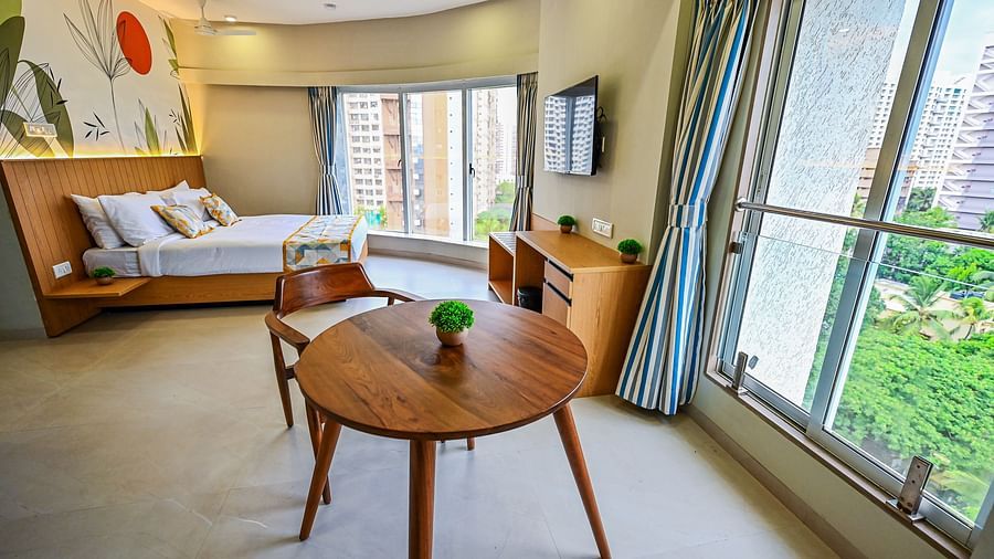 An image of Cozy Double Studio Room featuring a bed, a cabinet, a chair and table set, and a large window at Indie Stays Studio, Chembur