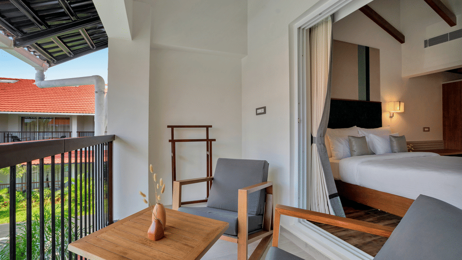 Balcony seating with chairs and a table beside glass doors showing the bedroom of Suite at Mango Hill, Velankanni.