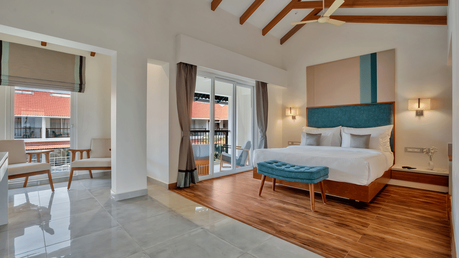 Bedroom area inside Suite at Mango Hill, Velankanni with a bed, bench, chairs, and glass door leading outside.