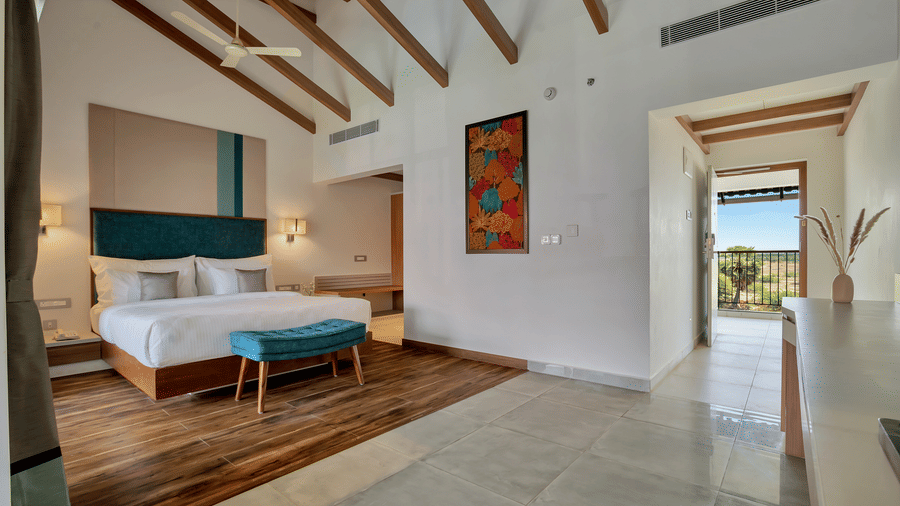 Interior of Suite at Mango Hill, Velankanni with a bed, bench, wall artwork, ceiling fans, and doorway.