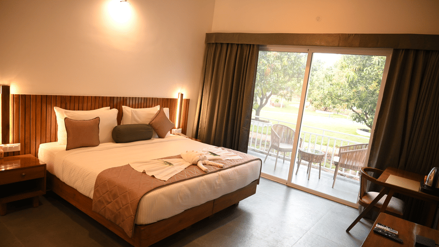A double bed alongside a sliding window with an outside view at the Deluxe Cottage at Mango Leaf Lake Resort, Pune