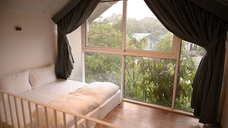 View of the greenery outside the window along with the Side view of the mattress in the attic of the Kutumbh Suite at Mango Leaf Lake Resort, Pune