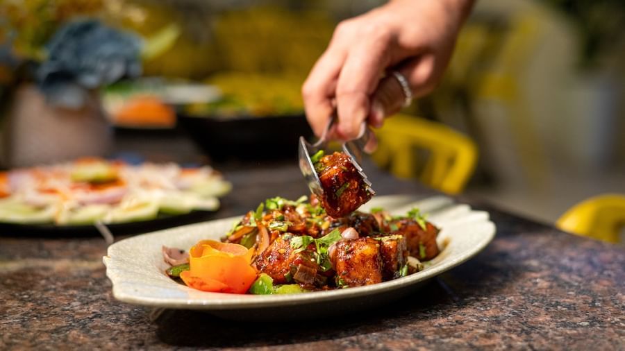 A waiter uses tongs to serve a portion of paneer from a platter at Pravasa Stay, Shirdi.