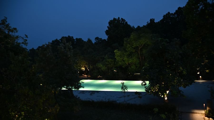 A view of the swimming pool at Saraca Resort & Spa Corbett at blue hour with the water inside the pool lit up