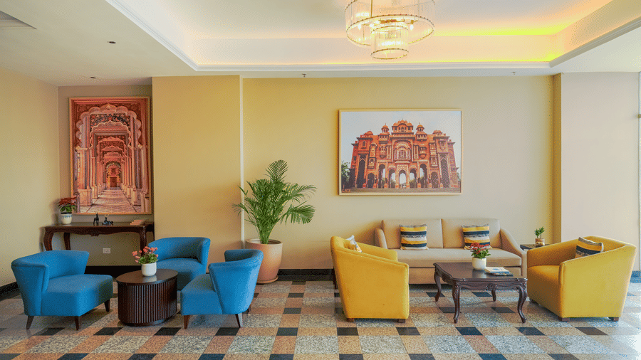 The brightly lit reception at Urban Suites by BluSalzz, Jaipur, with a tiled floor, featuring seating arrangements, low tables, and a wall mounted painting.