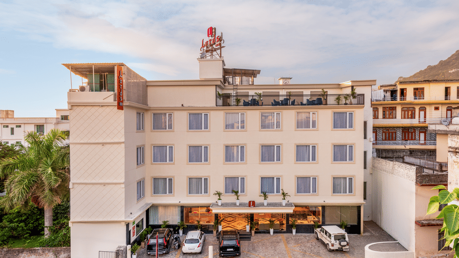 Exterior view of Lords Inn Katra, one of the ideal Katra hotels, Vaishno Devi, showing a multi storey white building with windows, a front parking area with cars, and a clear sky.