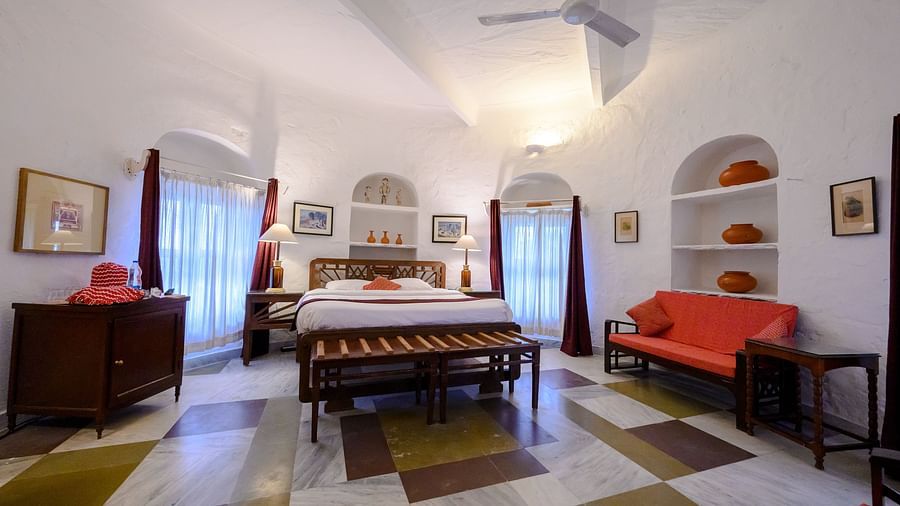 Hill Fort Kesroli 14th Century Alwar - interior view of the Mubarak Mahal room with a queen size bed, a ceiling fan and a red sofa with paintings on the wall