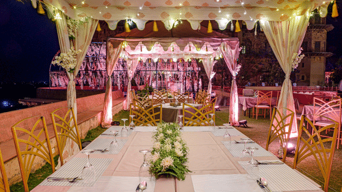 A long table set with cutlery and flowers under a tented structure, with chairs, at Tijara Fort-Palace - 19th Century, Alwar.