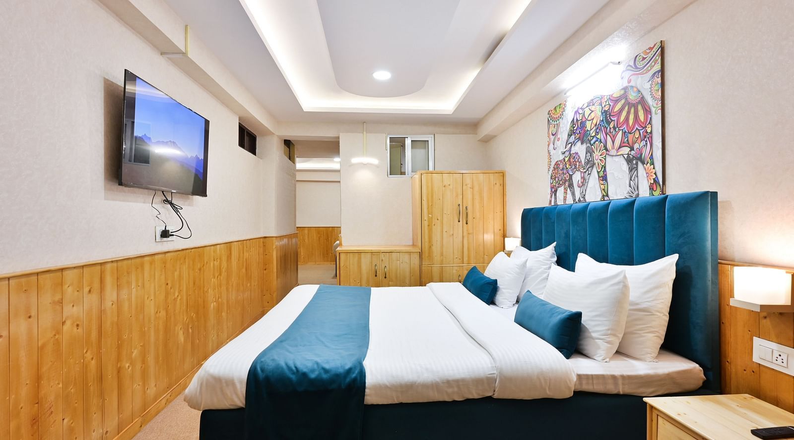 Family room with a king size bed, wooden cupboards, wooden bedside table with bright lighting, and a wall-mounted television at Avianna Seven Seas, Darjeeling2