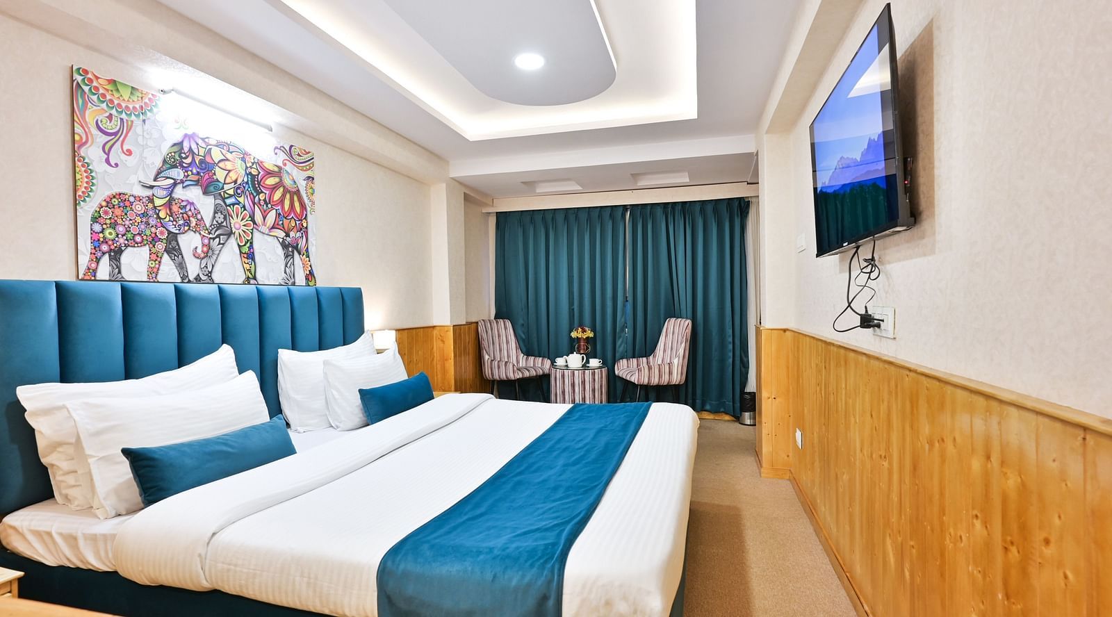 Family room with a king size bed, wooden cupboards, wooden bedside table with bright lighting, and a wall mounted television at Avianna Seven Seas, Darjeeling3