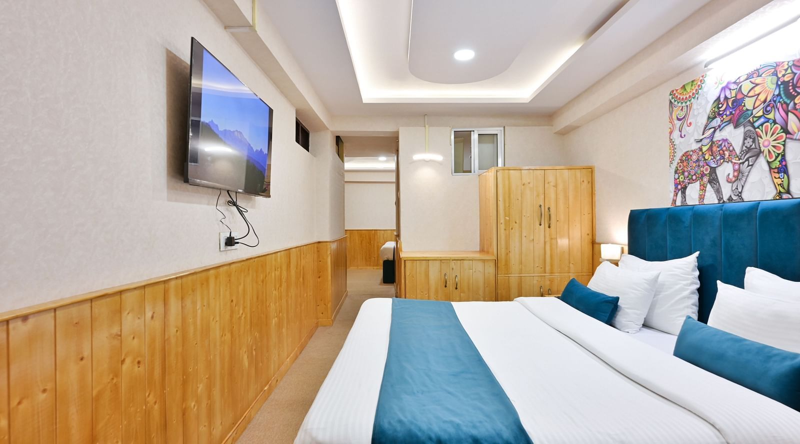 Family room with a king size bed, wooden cupboards, wooden bedside table with bright lighting, and a wall-mounted television at Avianna Seven Seas, Darjeeling5