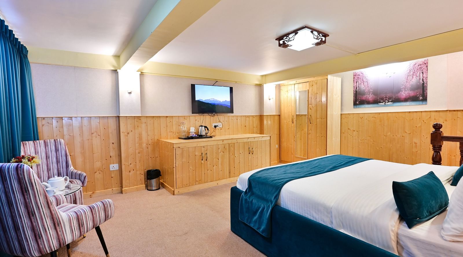 Premium room featuring a king sized bed, wall mounted television, windows with curtains, and warm lighting at Avianna Seven Seas, Darjeeling18