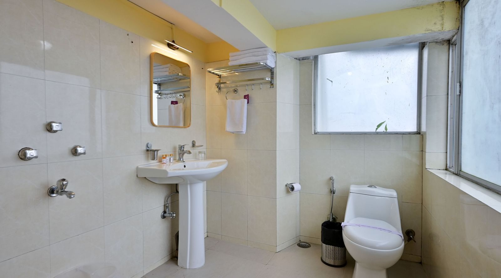 The spacious bathroom in the Premium Room is equipped with a washbasin, mirror, geyser, and western toilet at Avianna Seven Seas, Darjeeling