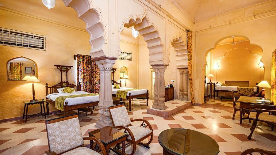 A room with multiple beds, seating areas, and arched architectural details at Tijara Fort-Palace - 19th Century, Alwar.