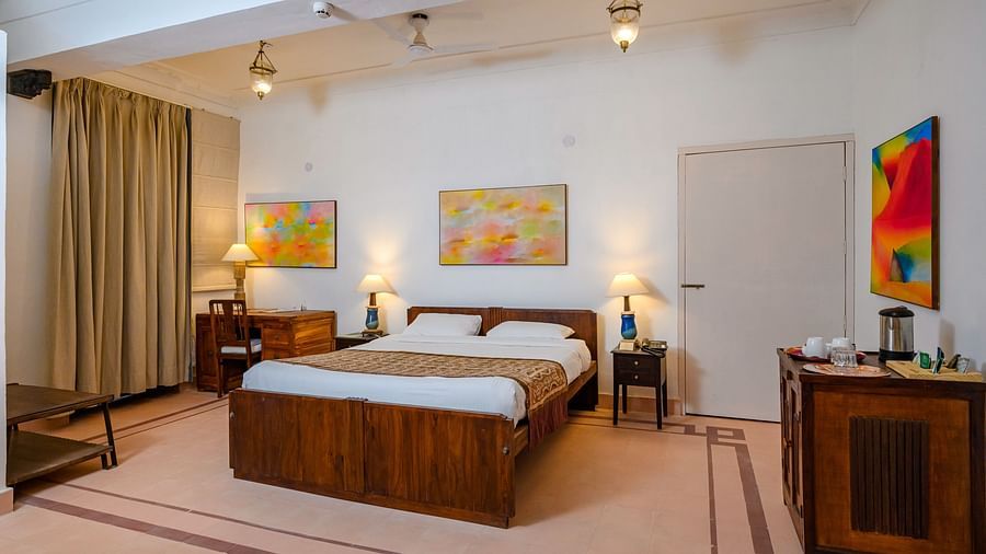 Tijara Fort-Palace - 19th Century, Alwar: Bedroom with a bed, bedside tables with lamps, a desk with a chair, artwork on the walls, and curtains.