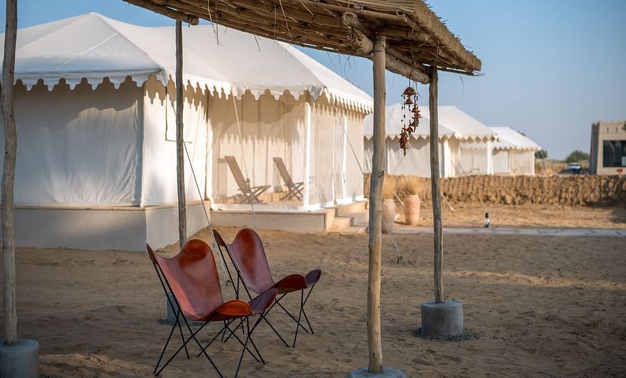 alt-text Foldable chairs are placed under a roofed area near the accommodations - Karwaan Jaisalmer