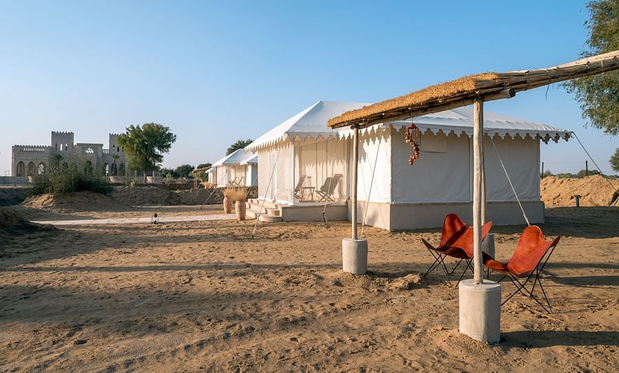 alt-text Foldable chairs are placed under a roofed area near the accommodations - Karwaan Jaisalmer