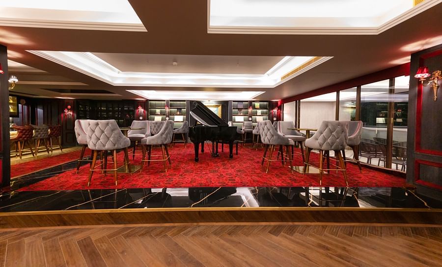 alt-text A platform with a tables and chairs placed around a giant piano in Stable restaurant - The Manor Luxury Apartment, Shimla 