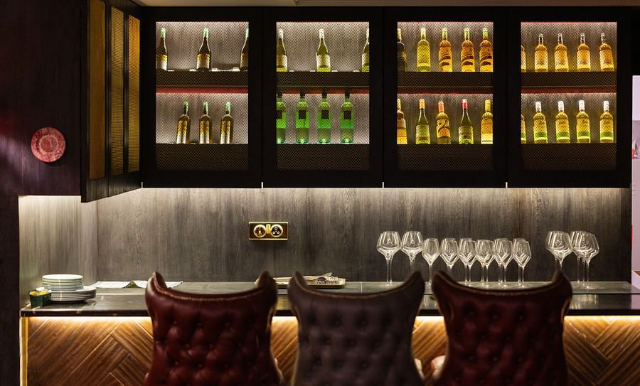 alt-text A bar counter at the restaurant with champagnes placed in cupboards - The Manor Luxury Hotel, Shimla