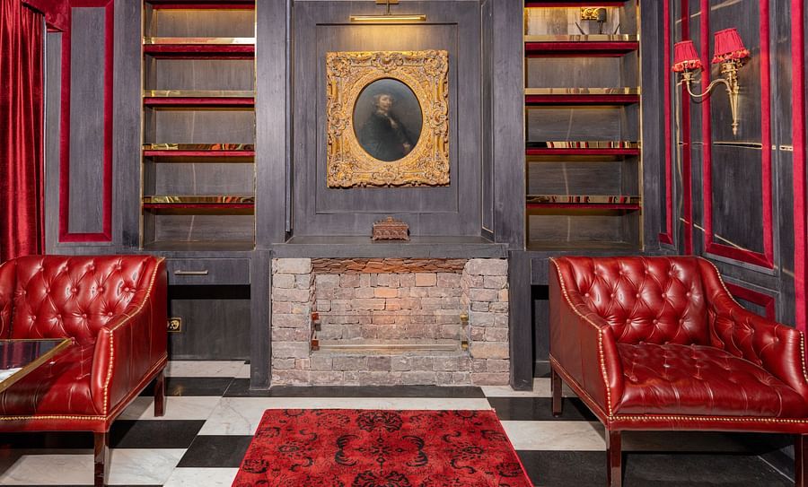 alt-text A couple of beautiful red chairs placed in front of a fire place with a vintage painting hanging on the wall - The Manor Luxury Hotel, Shimla