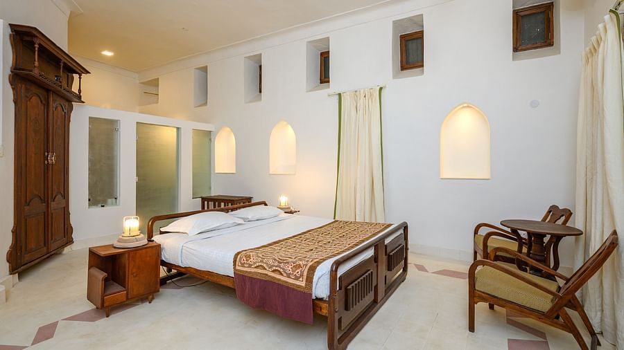 Tijara Fort-Palace - 19th Century, Alwar: Bedroom with a bed, bedside table, wardrobe, seating area with a table and chairs, and arched niches in the walls.