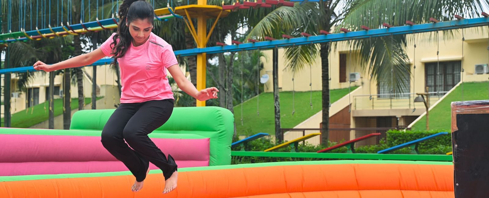 A person in a pink shirt jumps on a colorful inflatable structure outdoors