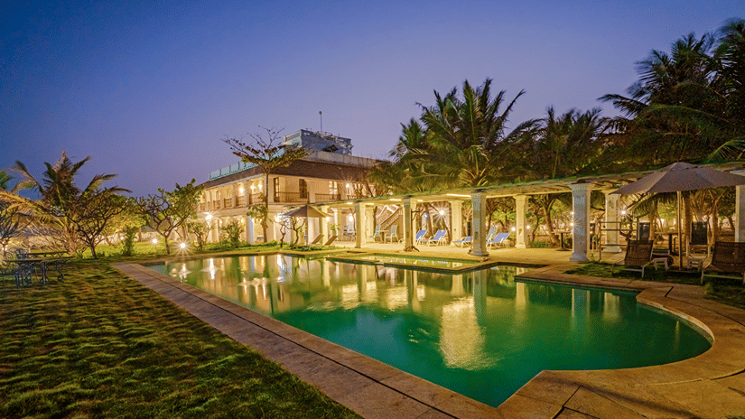 The Bungalow On The Beach in Tranquebar under a vibrant sky near Poompuhar with the pool reflecting the building as the dusk approaches