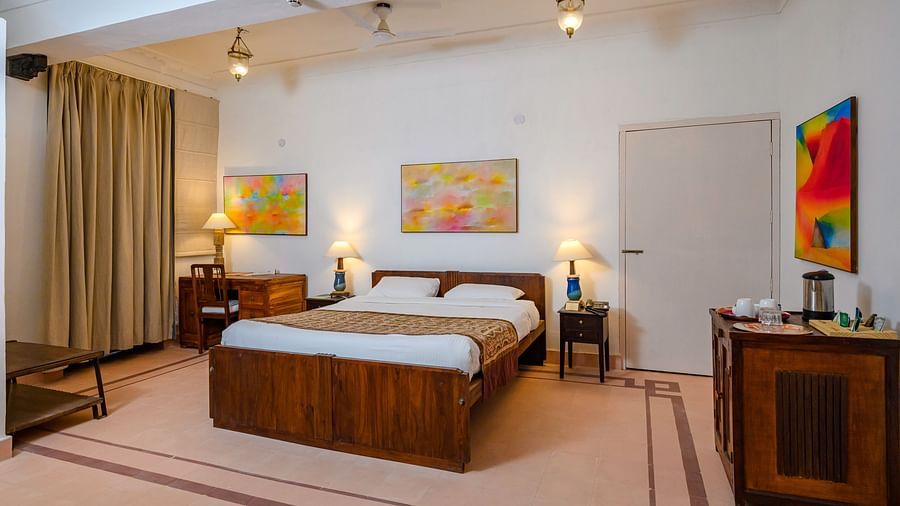 Tijara Fort-Palace - 19th Century, Alwar: Bedroom with a bed, bedside tables with lamps, a desk with a chair, artwork on the walls, and curtains.