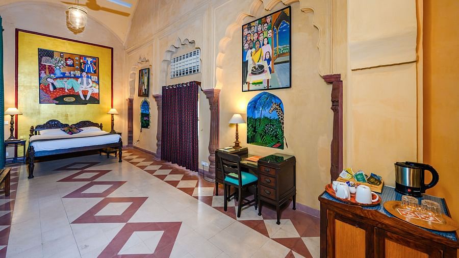 A spacious room with a bed, artwork, seating, and a refreshment station at Tijara Fort-Palace - 19th Century, Alwar.