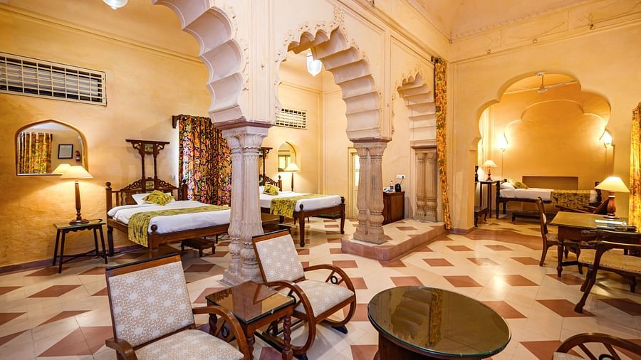 A room with multiple beds, seating areas, and arched architectural details at Tijara Fort-Palace - 19th Century, Alwar.