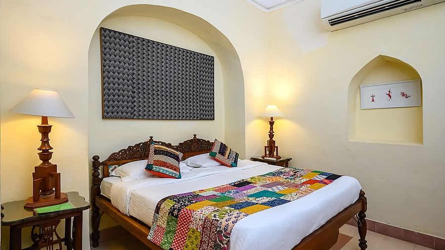 A bedroom with a bed, patterned artwork, an air conditioner, and arched alcoves at Tijara Fort-Palace - 19th Century, Alwar.