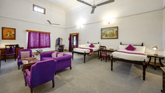 Twin beds, purple coloured sofas with a coffee table in the centre inside Maharaja Karam Singh room - The Baradari Palace