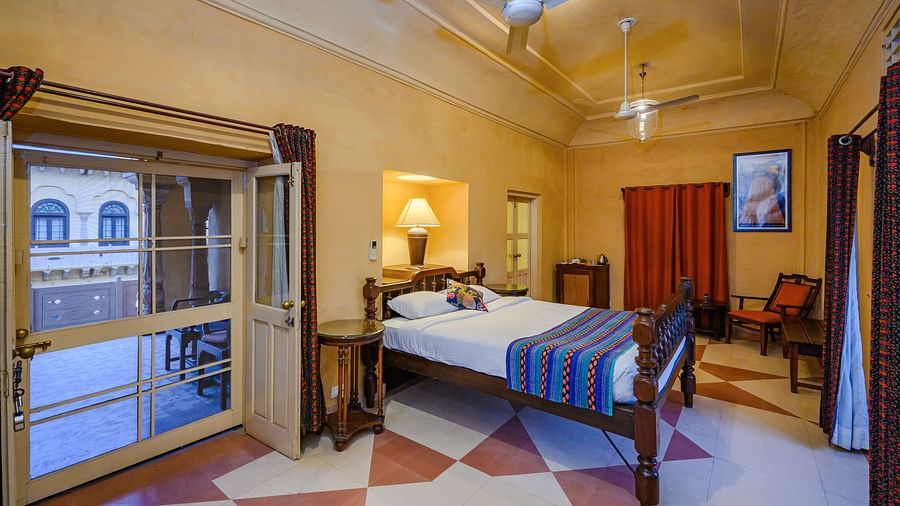 A bedroom with a bed, seating, and a glass door leading to a balcony at Tijara Fort-Palace - 19th Century, Alwar.