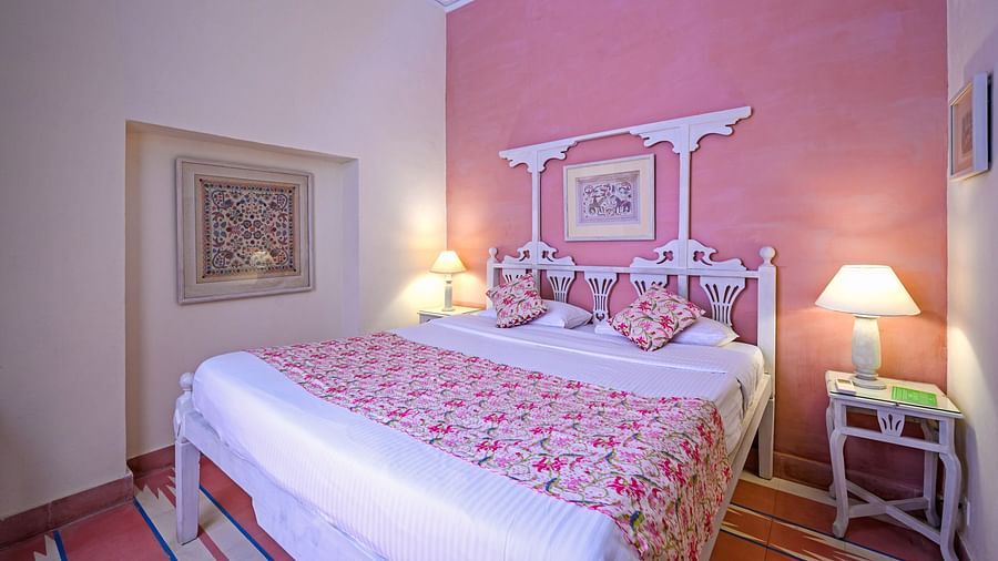 A bedroom with a bed, patterned bedspread, artwork on the wall, and a decorative headboard at Tijara Fort-Palace - 19th Century, Alwar.