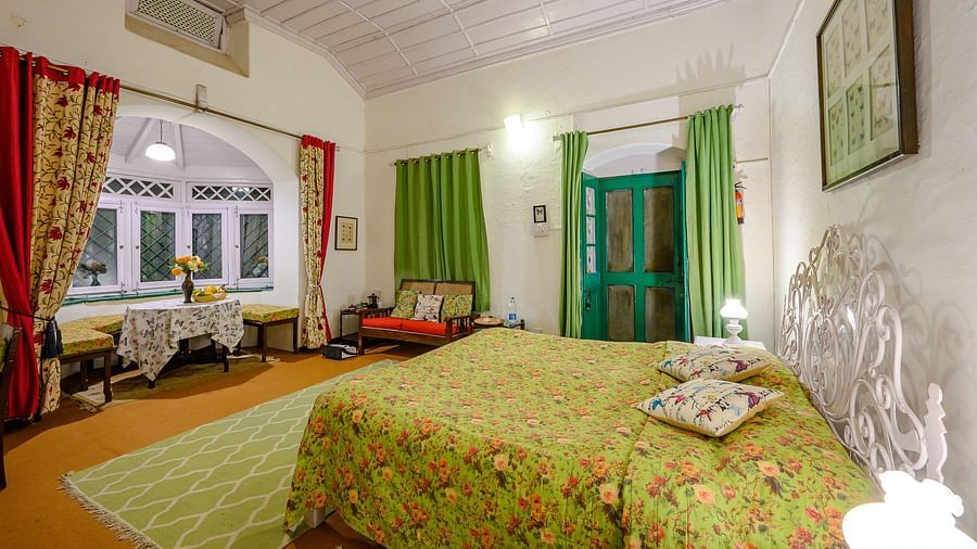Butterfly room side view with a double bed and a wide window overlooking the mountains, featuring a white wooden ceiling - Ramgarh Bungalows, Nainital.