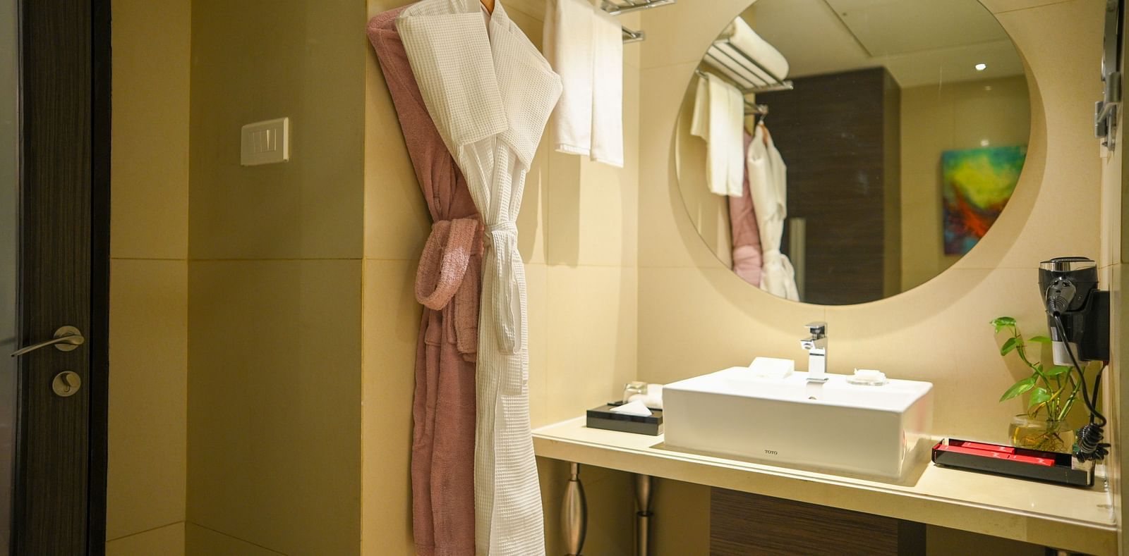 A bathroom image showcasing hanging pink and white bathrobes, a mirror, a sink, a hair dryer, and neatly arranged towels.