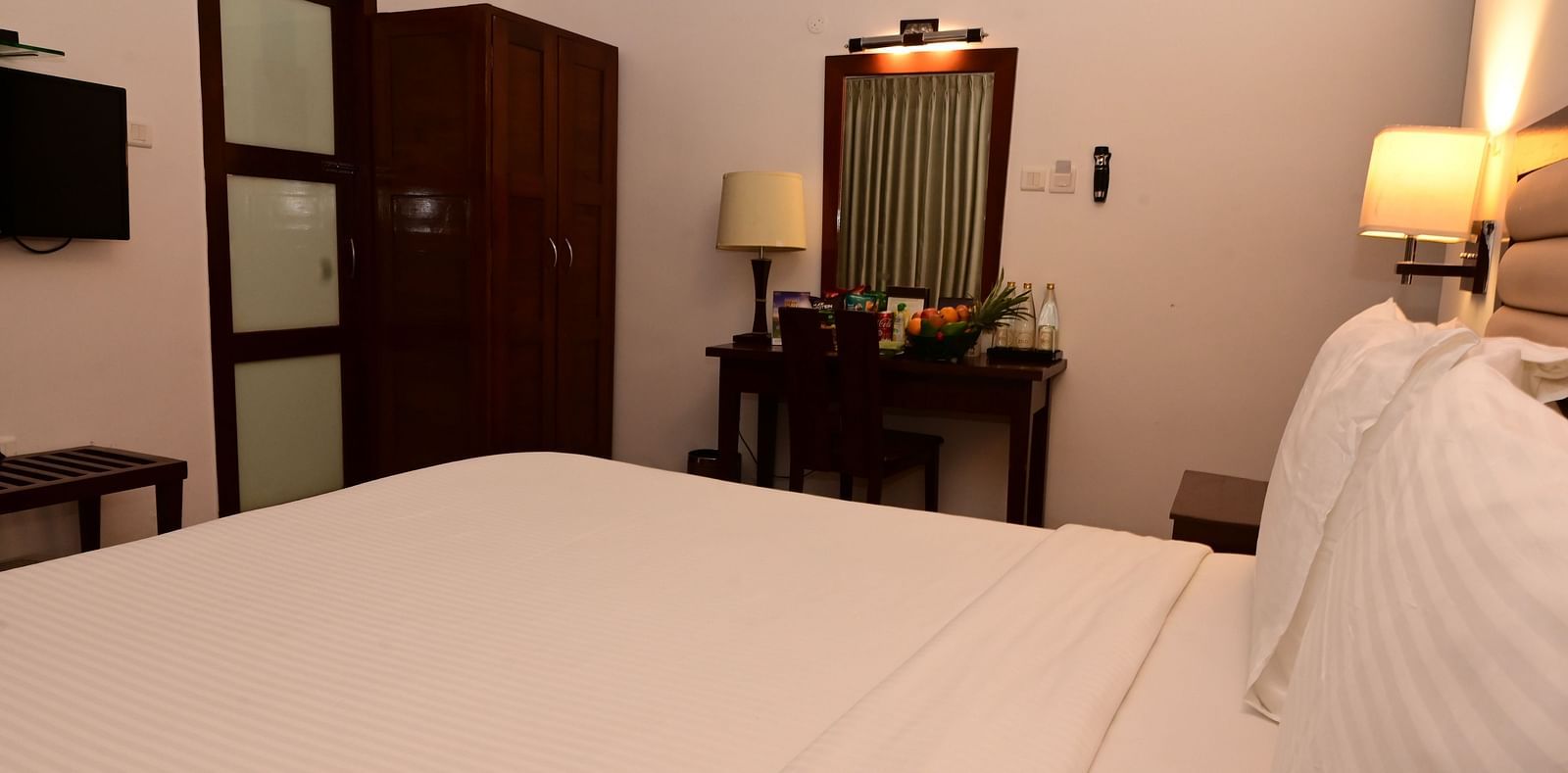 An image of a room with a king size bed, bed side table, lamps, dressing table, and a chair - GReaT trails Kodaikanal by GRT Hotels