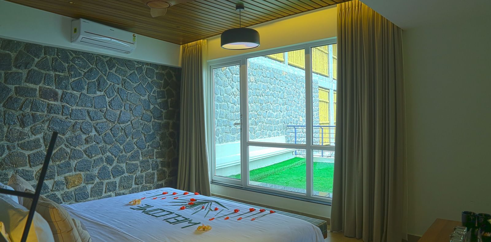 An angle of the pent house room with a bed and a sliding glass door leading to the turf - Great Trails Yercaud by GRT Hotels