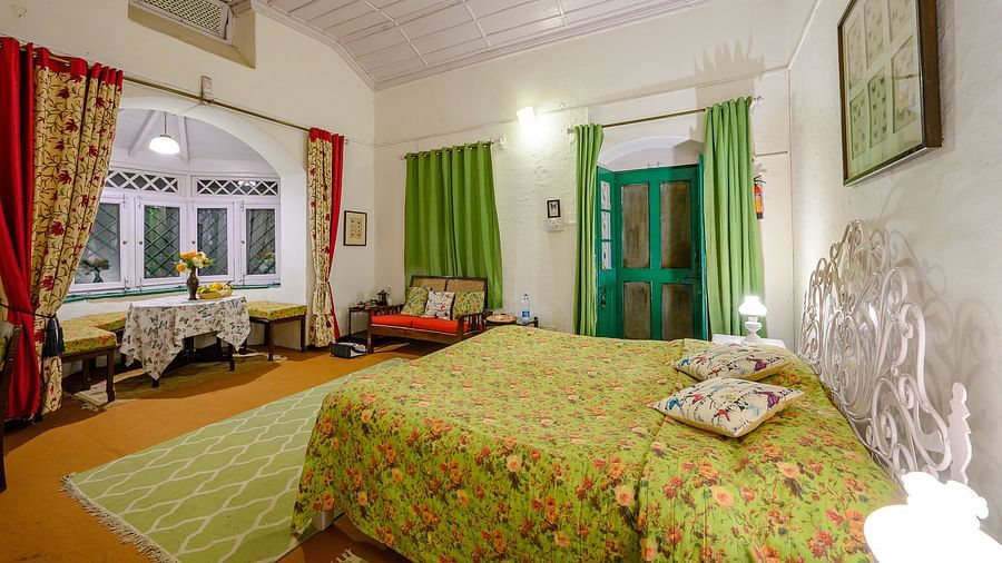Butterfly room side view with a double bed and a wide window overlooking the mountains, featuring a white wooden ceiling - Ramgarh Bungalows, Nainital.