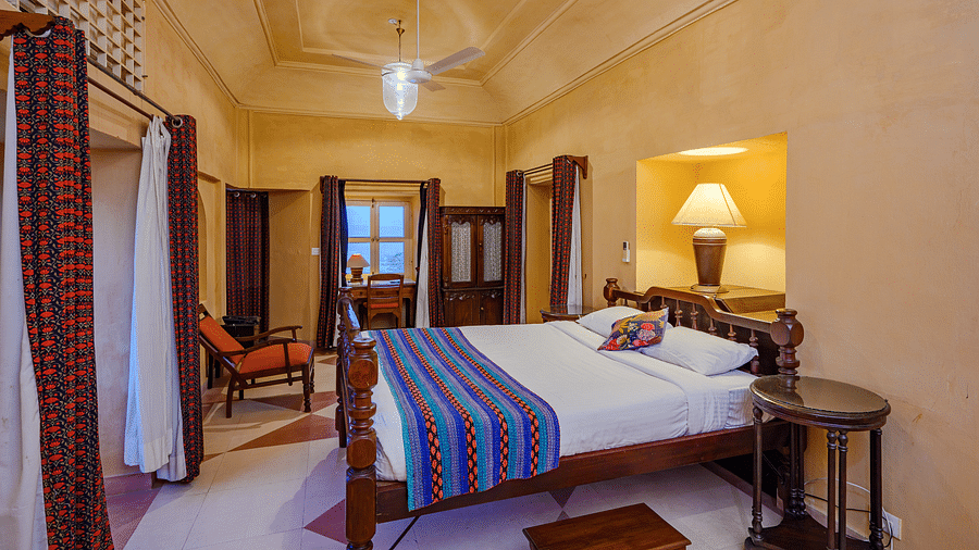 A bedroom with a bed, a seating area, and a decorative fabric panel at Tijara Fort-Palace - 19th Century, Alwar.