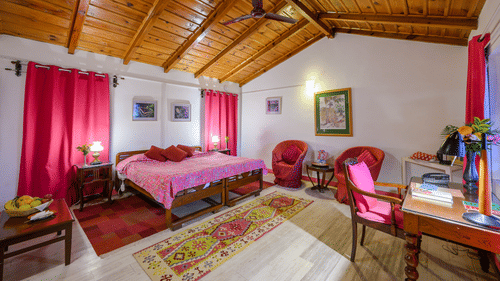 A pink themed Fucia Room with a work desk facing the window and a coffee table with fruit basket and room amenities like a telephone and an electric kettle - Ramgarh Bungalows, Nainital.