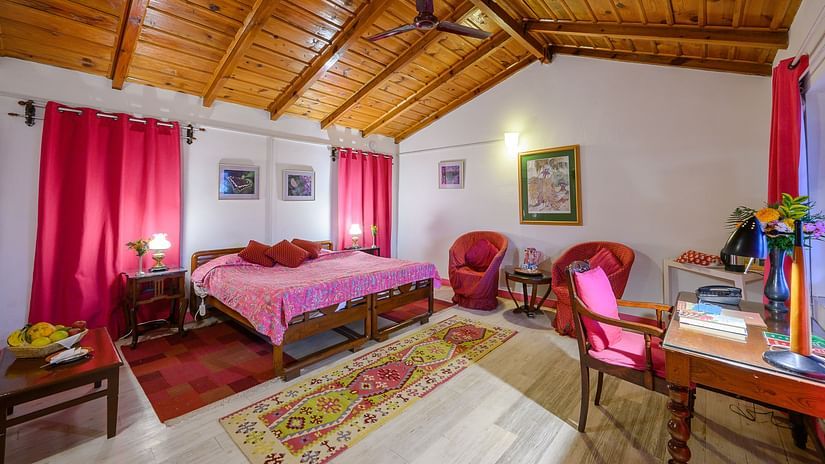 The Ramgarh Bungalows - a pink themed Fucia Room with a work desk facing the window and a coffee table with fruit basket and room amenities like a telephone and an electric kettle